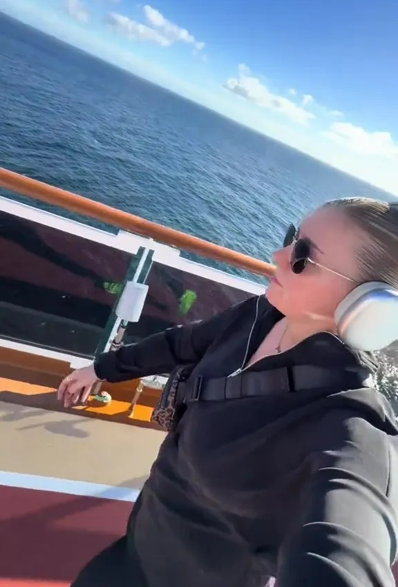 A woman on a cruise ship wearing headphones and sunglasses, looking out at the ocean.