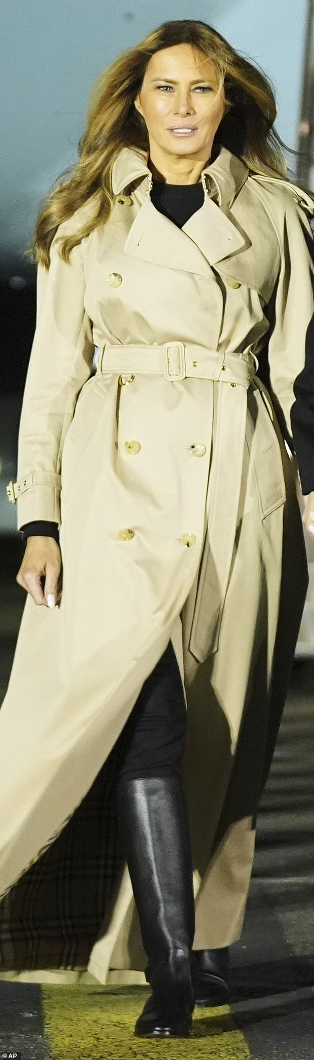 Melania is seen in a Burberry trench coat and Christian Dior black boots Saucer as she arrives at Stansted Airport