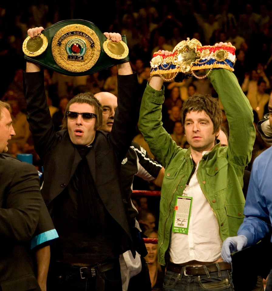 Noel and Liam Gallagher holding boxing championship belts in the ring.