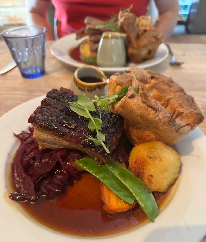 Plates of roast pork, gravy, Yorkshire pudding, and vegetables at a pub.