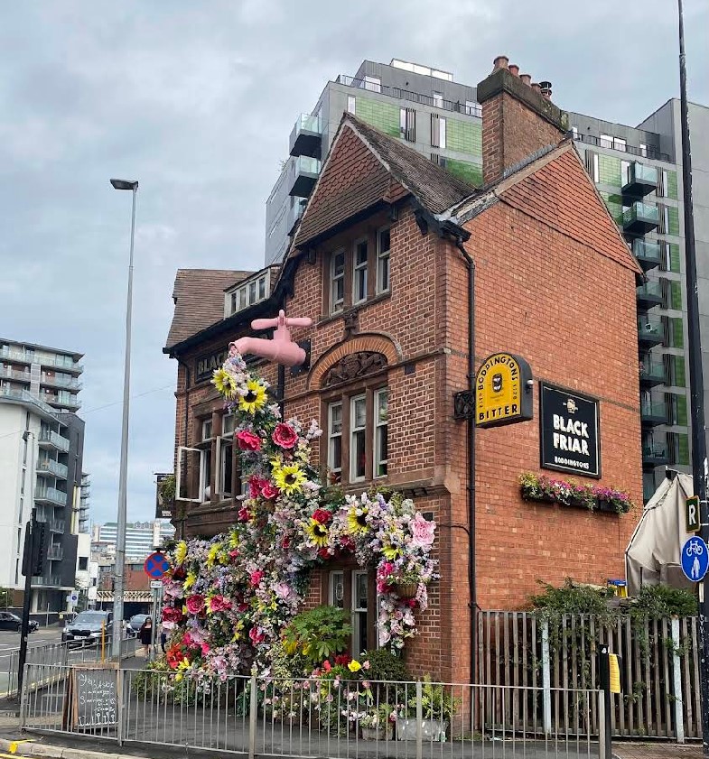The Black Friar pub in Salford, England, with an elaborate floral display and a large pink tap installation on its facade.