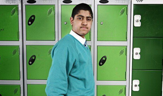 A young man in a school uniform is looking at a laptop.