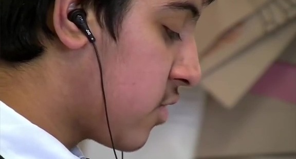 A young person with dark hair wearing wired earbuds in their right ear, seen in profile with their eyes closed.