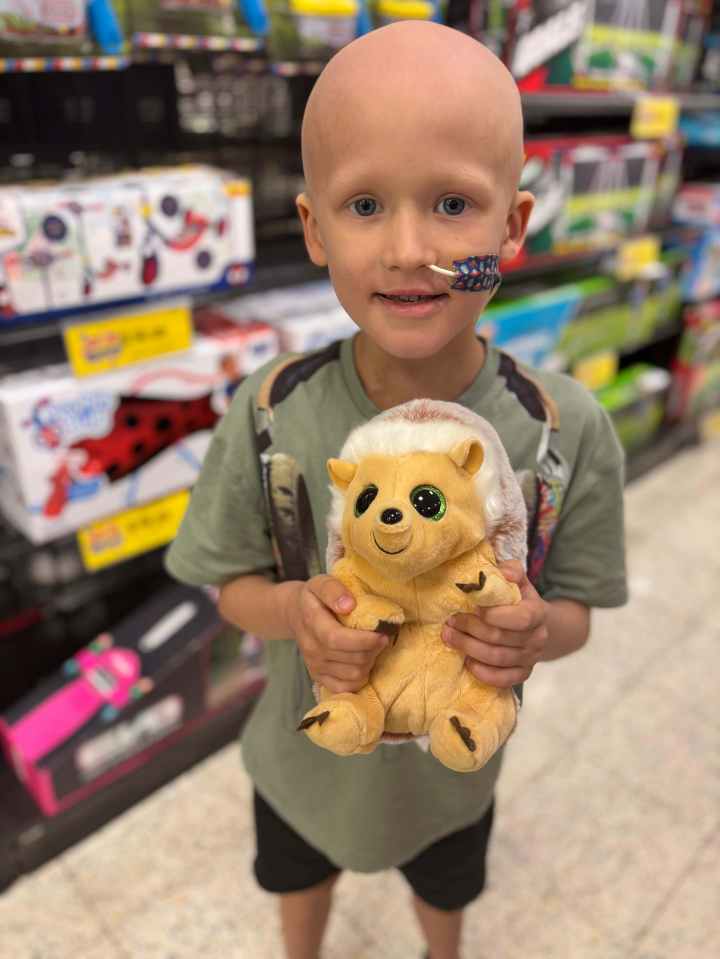 Tommy, a child with cancer, holding a hedgehog stuffed animal in a store.