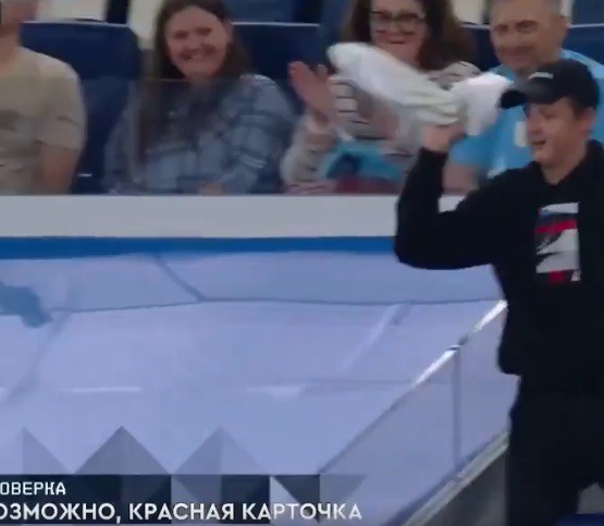 Spectator in black hoodie and cap with raised hand and white towel.