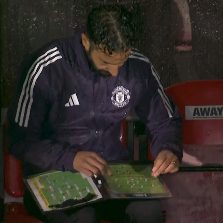 Manchester United coach looking at tactics board in the rain.