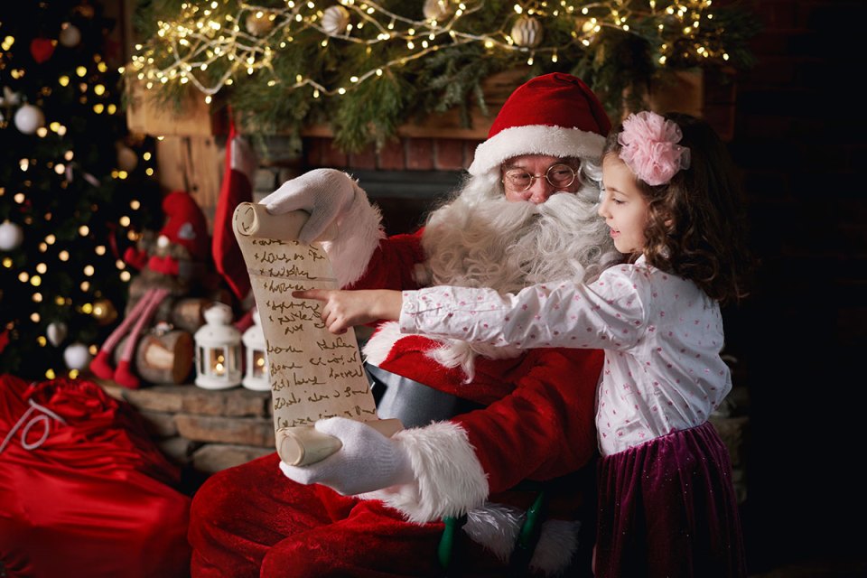 Santa Claus with a little girl pointing at his scroll.