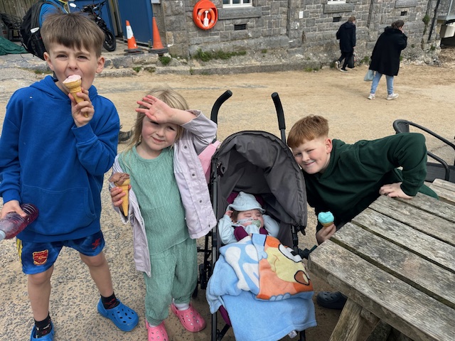 Three children eating ice cream with a baby in a stroller.