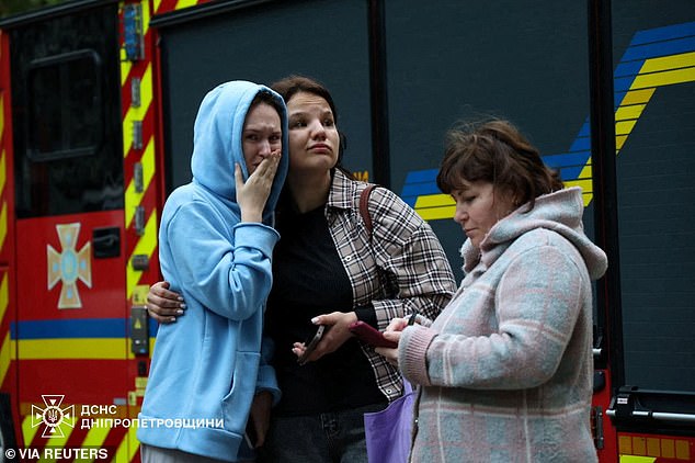 Ukrainian residents react as they stand near a residential building damaged during a Russian missile strike
