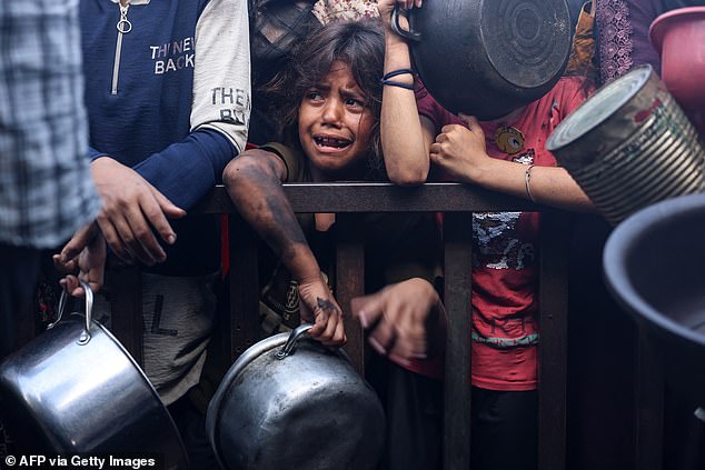 A young girl reacts as displaced Palestinians elbow their way in front of a community kitchen in Khan Yunis in the southern Gaza Strip on September 19, 2025