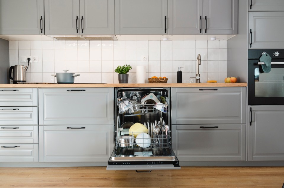 Open dishwasher in a modern kitchen, with dishes and cutlery inside.