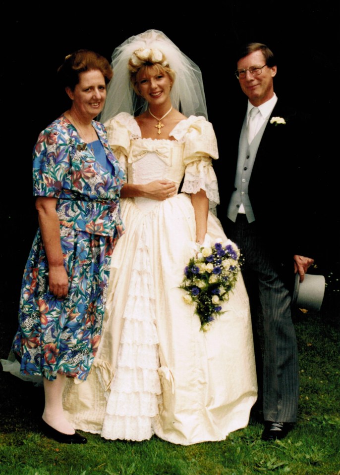 A bride, groom, and a woman in a floral dress posing for a wedding photo.