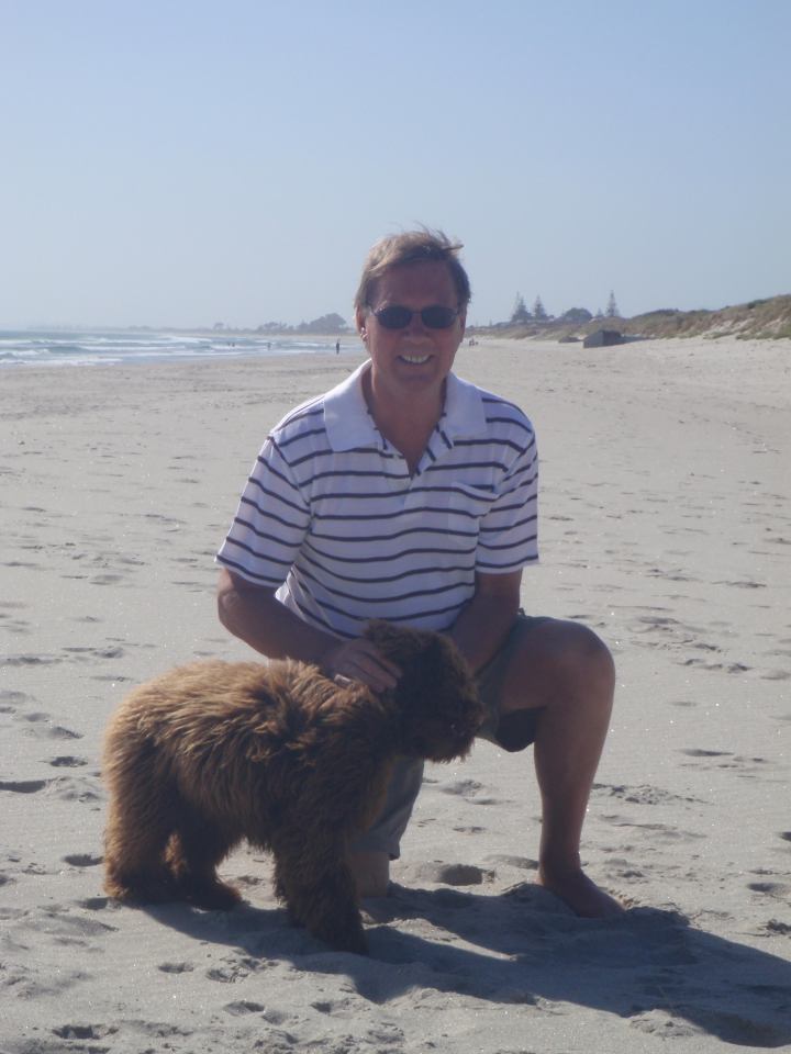 Man kneeling on a beach with a brown dog.