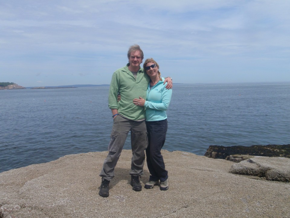 Couple standing on rocks by the ocean.