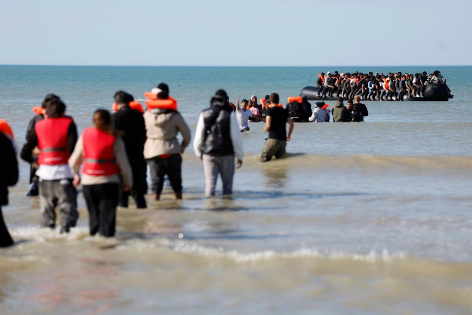 Migrants wading into the water to board a small boat.