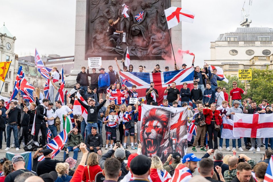 People at a "Unite the Kingdom" gathering in Trafalgar Square, some holding Union Jack flags and signs that read "Stop Importing Start Deporting" and "This is a Christian Land."