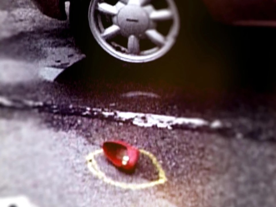 A single red shoe on the ground, circled in yellow chalk, next to a car tire.