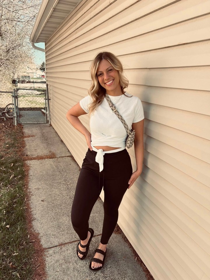 Raylee Reinhart posing outdoors, leaning against a house with light-colored siding.