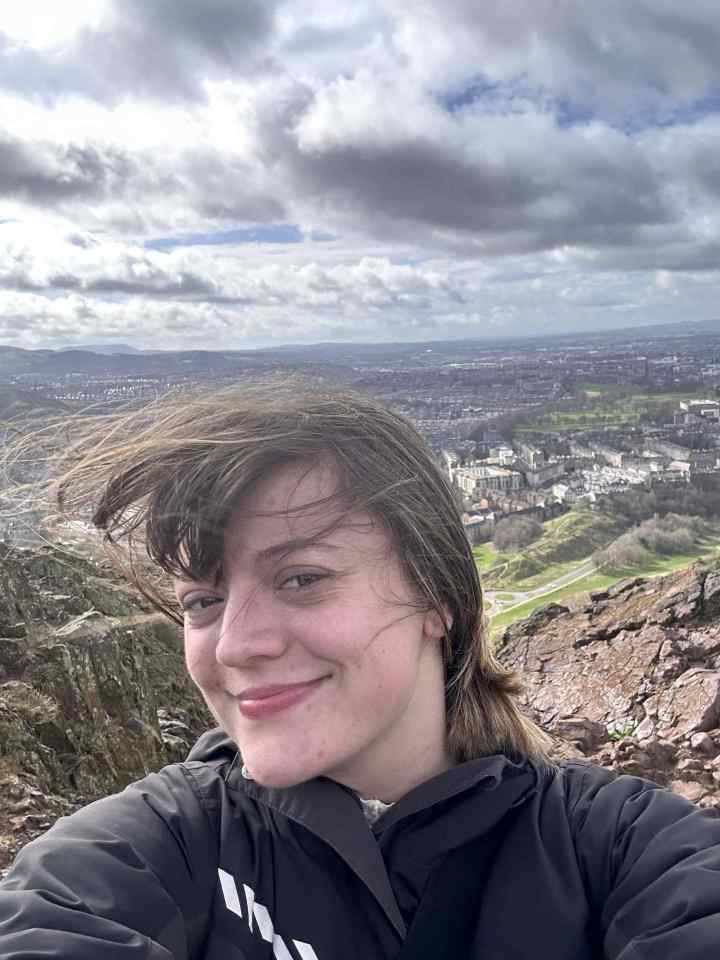 Woman smiling on a mountaintop overlooking a city.