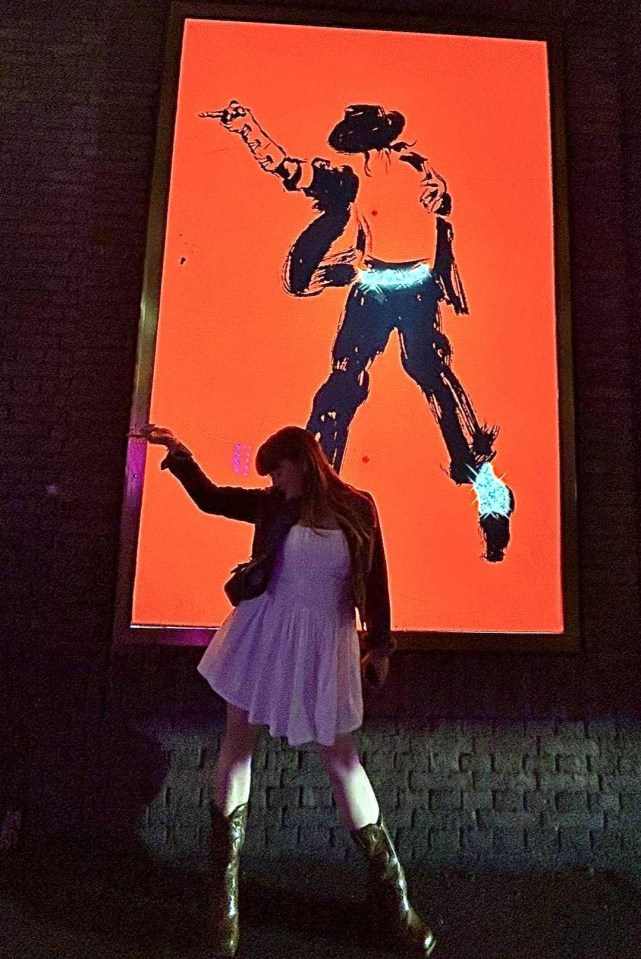 Woman in a white dress posing next to a large Michael Jackson mural.