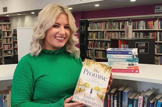 Emma Heatherington holding her book, "The Promise," in a library.