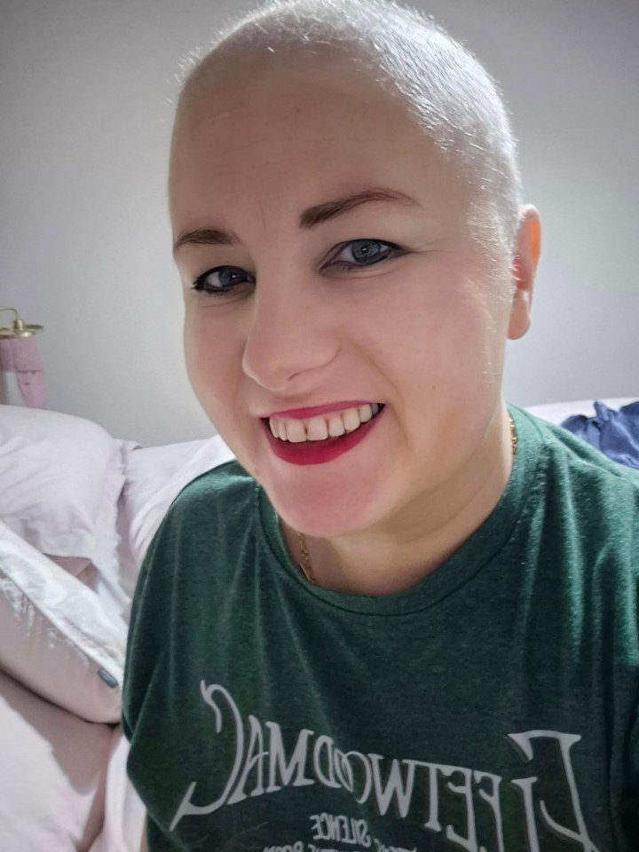 Close-up portrait of a smiling woman with a shaved head.