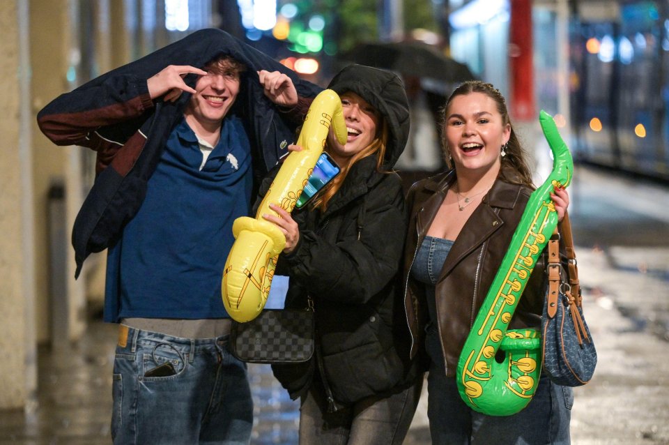 Three people with inflatable saxophones smiling, with one using his jacket as a hood.