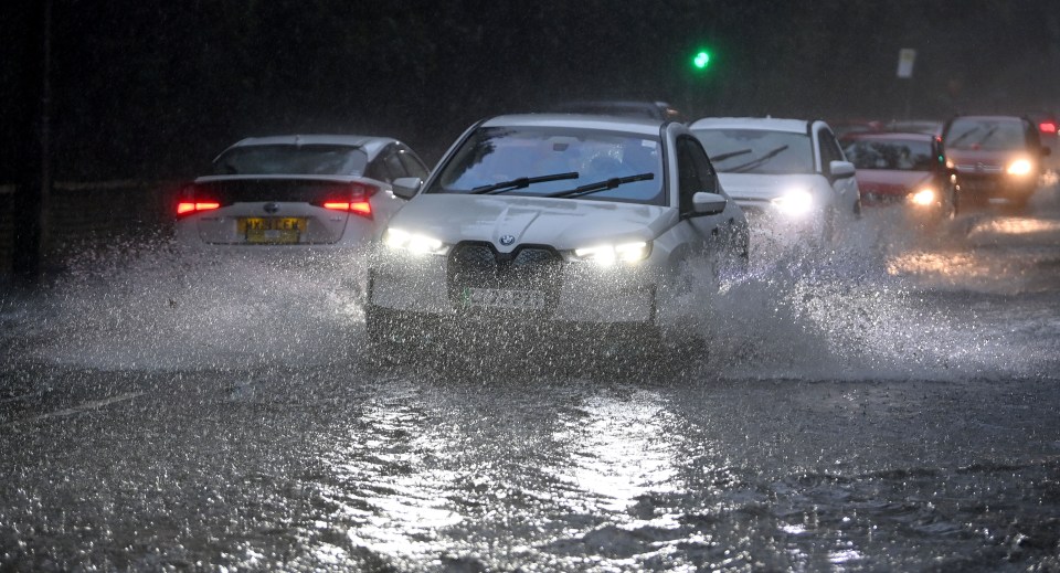 Cars driving through floodwaters on Brooklands Road in Sale, Manchester.