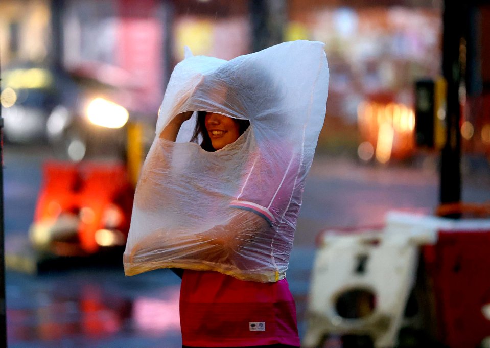 A smiling woman wearing a pink shirt and using a plastic bag as a makeshift hood during a rainy night in Leeds.