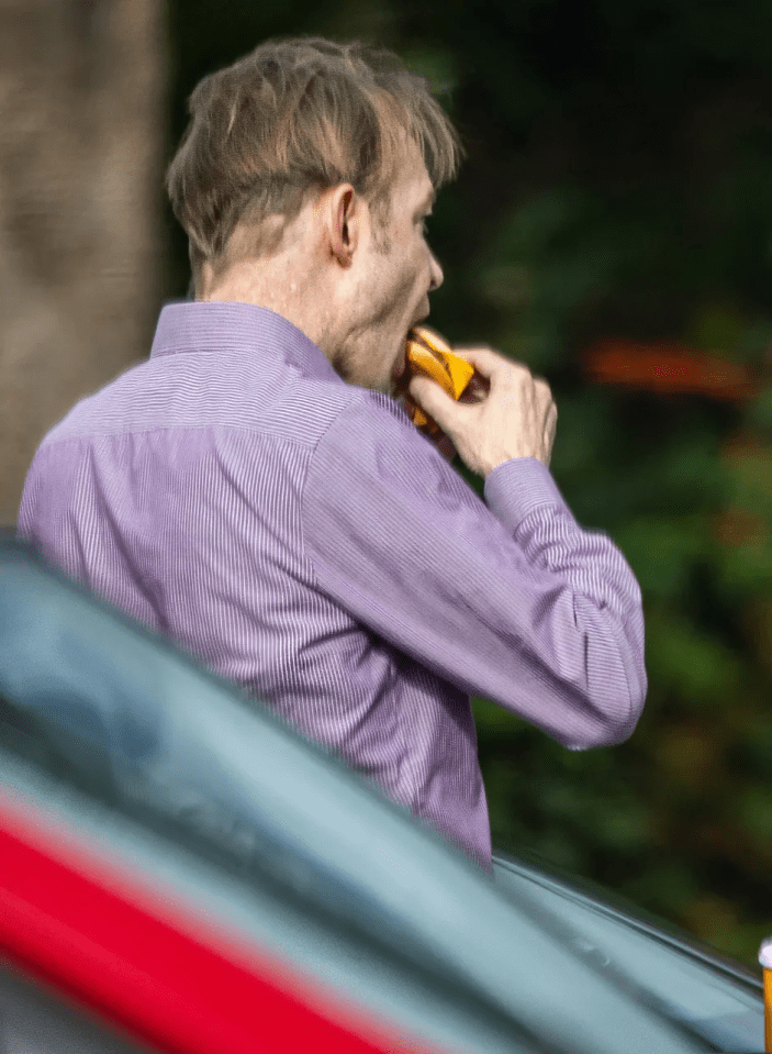 A man in a striped purple shirt eating a yellow packaged item.