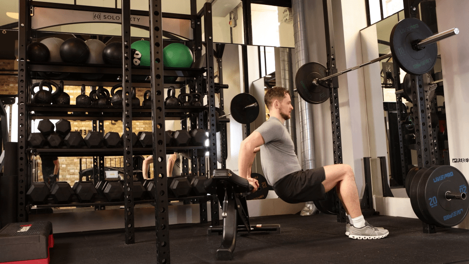 A man performs a tricep dip using a weight bench in a gym.