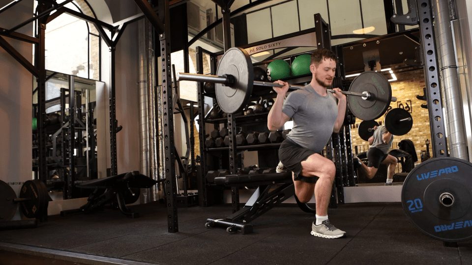 Man performing lunges with a barbell in a gym.