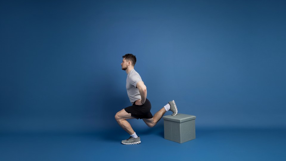 A man performing a Bulgarian split squat, with one foot elevated on a gray box.