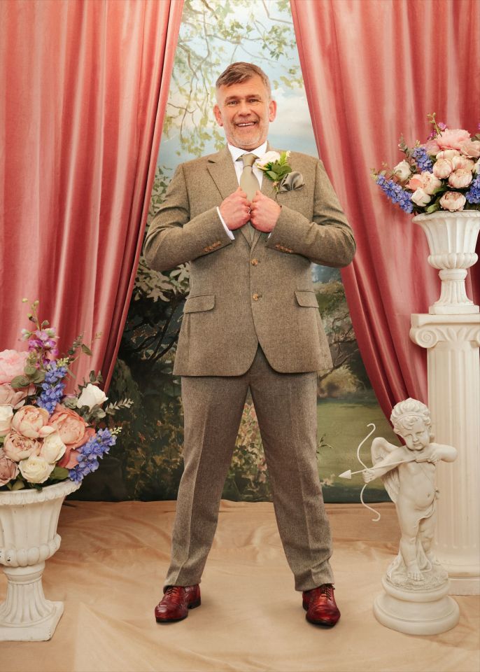 Paul, a middle-aged man with graying hair and a beard, stands in a light brown tweed suit, holding his lapels and smiling at the camera.