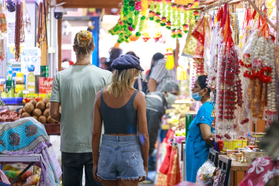 A couple walking through a market with colorful garlands and other items hanging for sale.