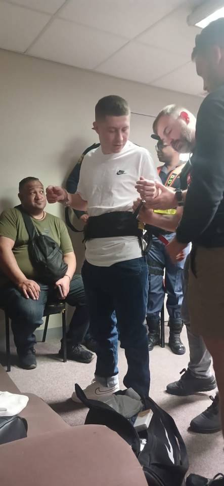 Man in white T-shirt and blue jeans being handcuffed by another man.