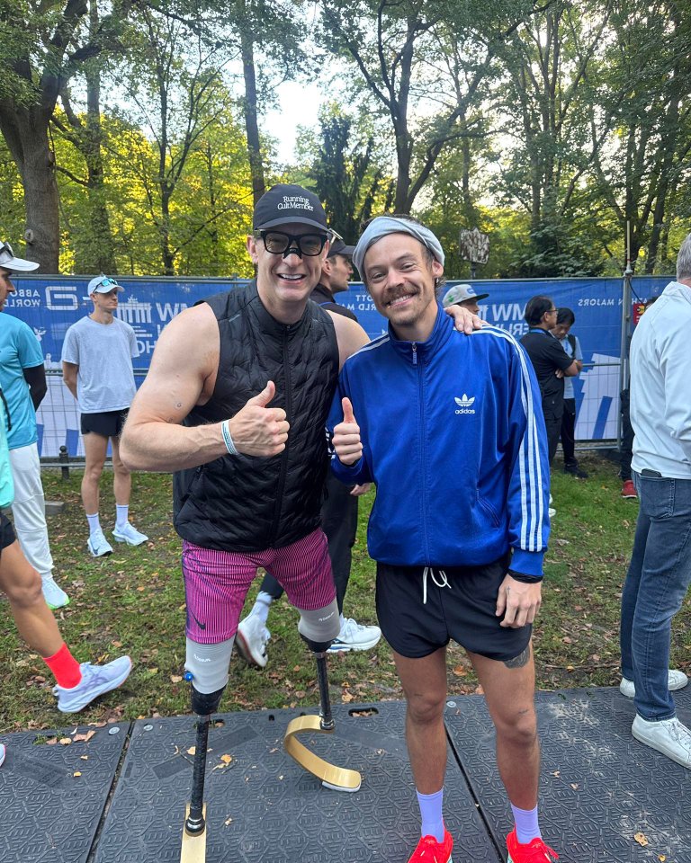 Harry Styles with an athlete who has prosthetic legs, both giving a thumbs-up.