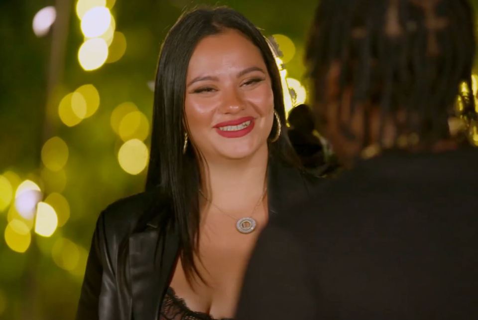 Linda De Sousa Abreu smiling in a black jacket and a necklace, looking at a person with dreadlocks.