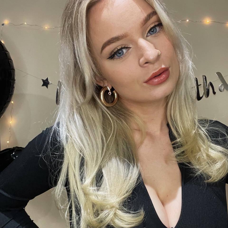 Blonde woman Aisha Golsby wearing a black top, golden hoop earrings, and eye makeup.
