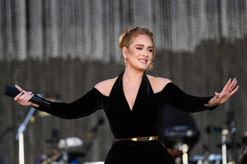 Adele performing on stage at Hyde Park, wearing a black off-the-shoulder gown with a gold belt.