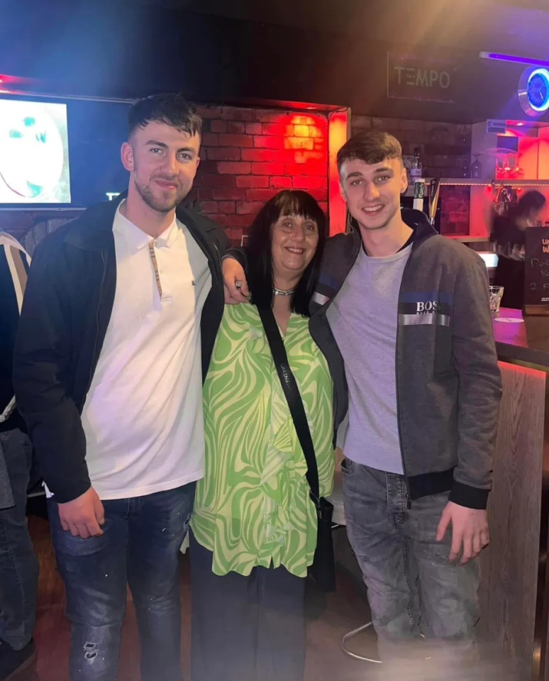 A woman stands between two young men in a dimly lit bar.