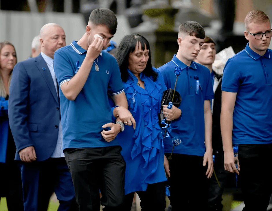 People in blue attire, some holding blue roses, at an event.