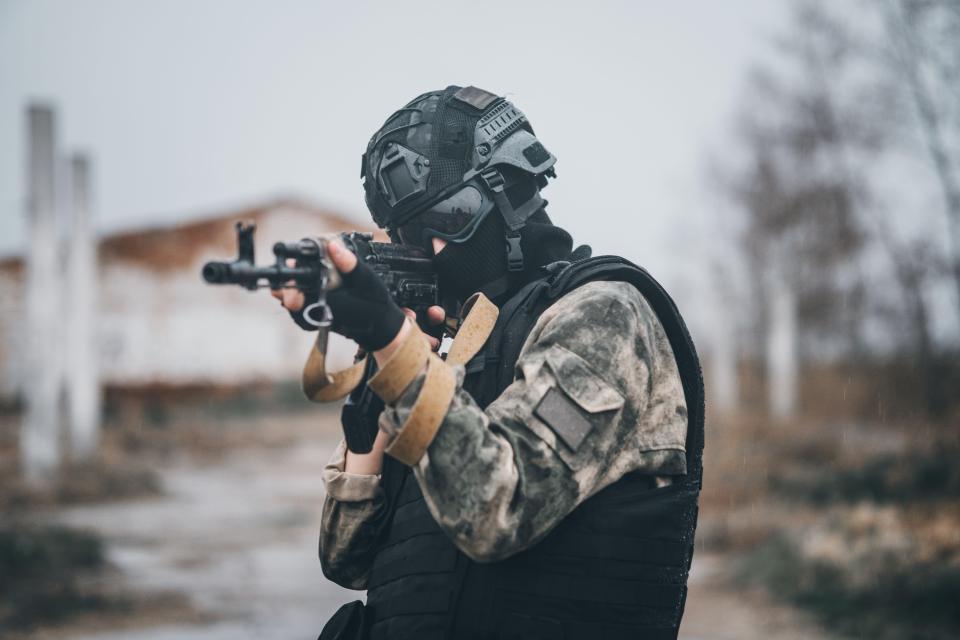 Special forces soldier in tactical gear aims a rifle.