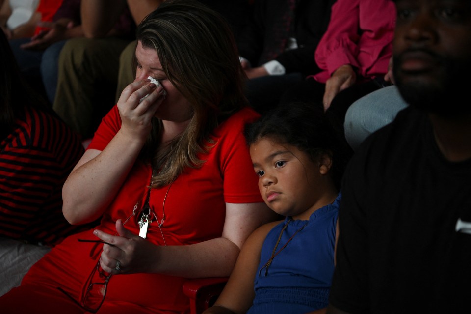 Shauna Griggs wiping her eye with a tissue as her daughter Peyton Griggs, 7, sits beside her at a memorial service.