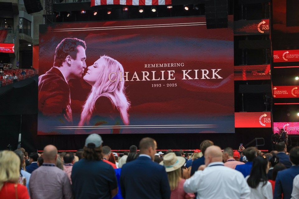 A memorial service at State Farm Stadium features a large screen displaying "Remembering Charlie Kirk 1993 - 2025" with a photo of him and a blonde woman.