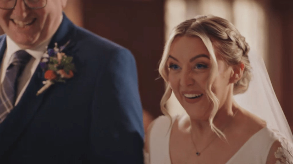 A smiling bride in a white dress next to a man in a blue suit and glasses.