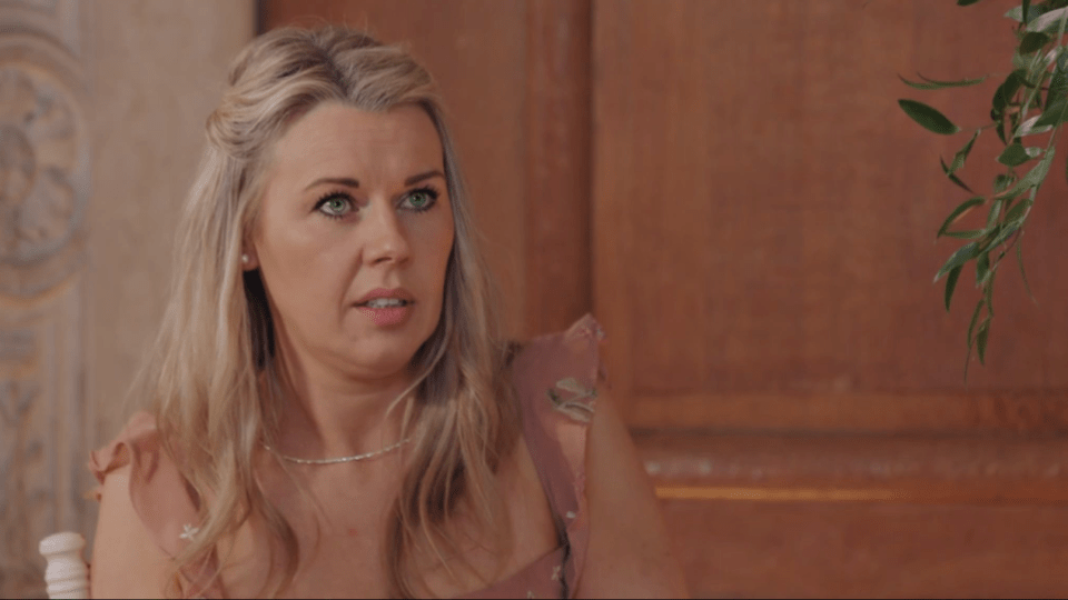 A woman with blonde hair and green eyes looks left with a surprised expression.