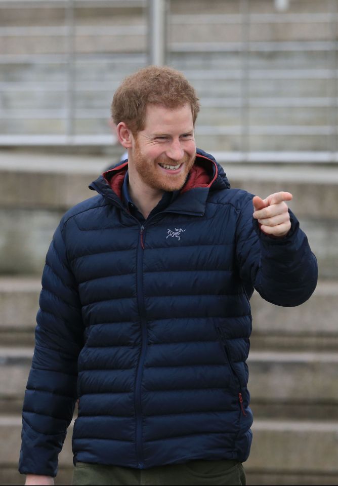Prince Harry in a navy puffer jacket, laughing and pointing.