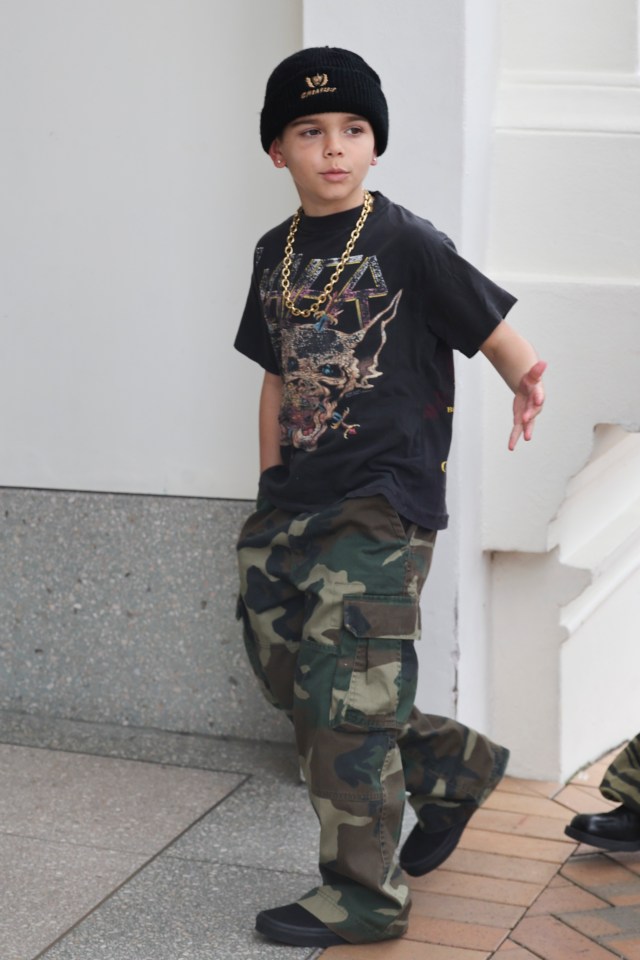 Reign Disick walking in camouflage pants, a black t-shirt, a gold chain, and a black beanie.