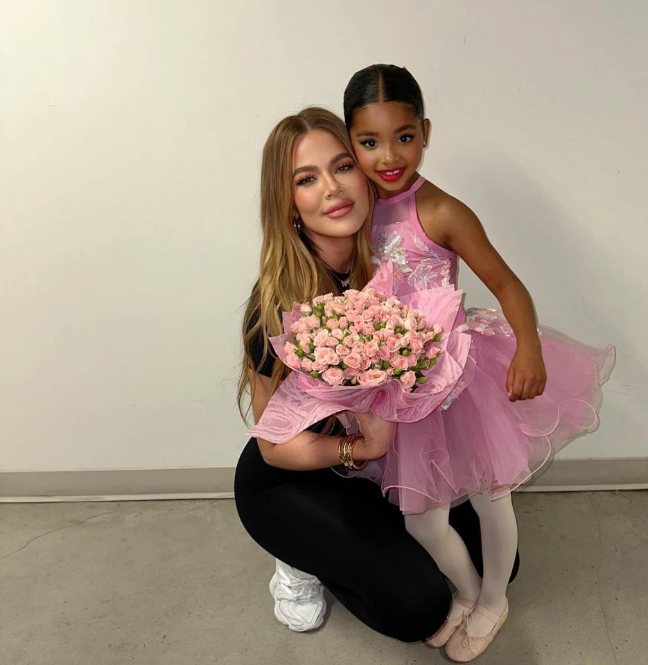 Khloe Kardashian with her daughter True, who is dressed in a pink ballet costume and holding a bouquet of pink roses.